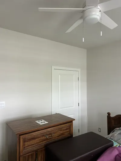 Bedroom corner with a vaulted ceiling, white ceiling fan, wood dresser, and a glimpse of the bed.