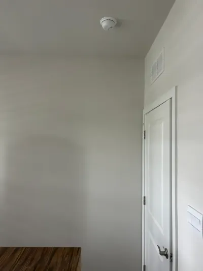 A hallway corner with a white door, wall vent, and ceiling-mounted smoke detector.