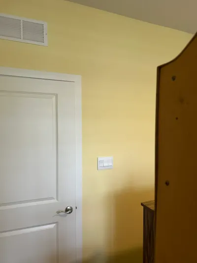 Yellow-painted wall with a white paneled door, light switch plate, and wooden furniture edge visible.