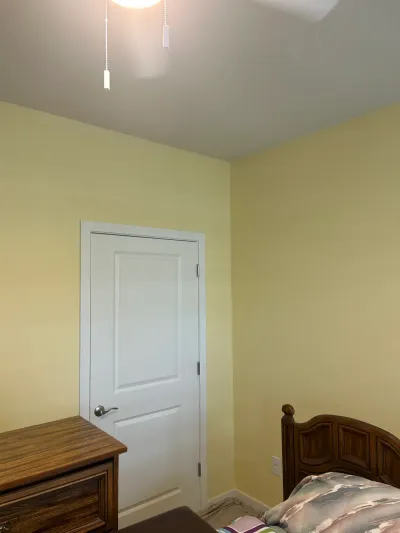 Corner of a yellow bedroom with a white closet door, wood furniture, and a pull-chain ceiling light.