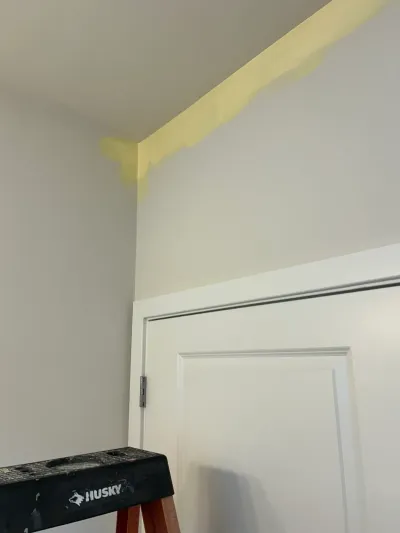A sloped ceiling corner with yellow paint edging above a white paneled door, with a step stool nearby.