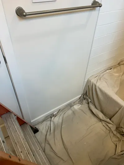 Bathroom mid-renovation with a glass panel, towel bar, ladder, and a drop cloth covering the tub.