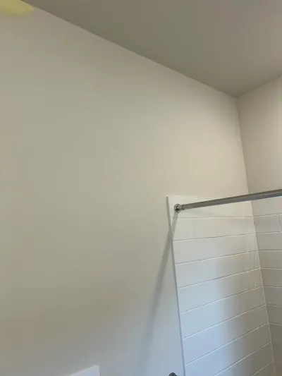 Corner of a bathroom shower with white subway tile and a chrome curtain rod against painted walls.