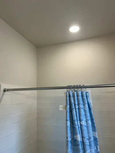 Corner of a tiled shower with a sloped ceiling, recessed light, and blue fish-print curtain.