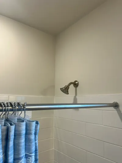 Close-up of a tiled shower corner with a brushed nickel showerhead and blue curtain.