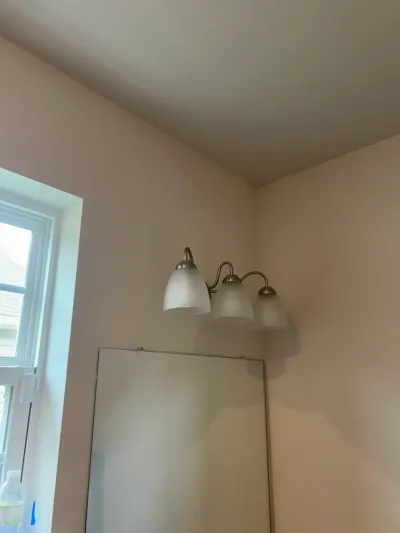 Close-up of a three-light bathroom vanity fixture with frosted glass shades above a mirror.