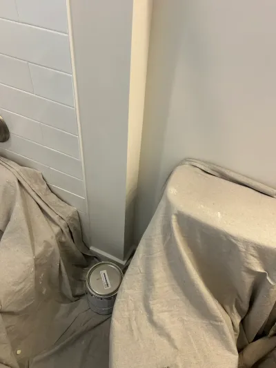Corner of a bathroom mid-renovation with subway tile, fresh paint, drop cloths, and a paint can.