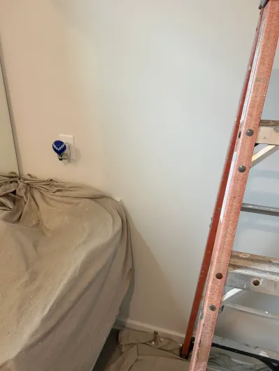 A covered piece of furniture and a ladder in a room being prepped for painting or renovation work.