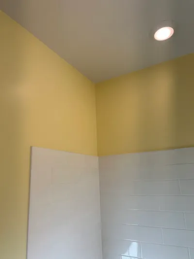 Bathroom corner with white subway tile wainscot, yellow walls above, and a recessed ceiling light.