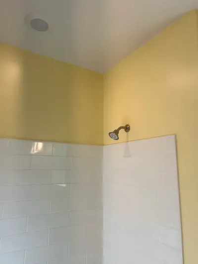 Shower corner with white subway tile, pale yellow walls above, and an oil-rubbed bronze shower head.