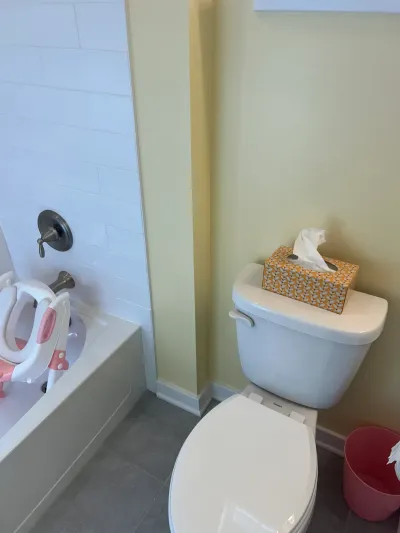 Small bathroom with white subway-tiled tub, white toilet, pale yellow walls and gray tile floor.