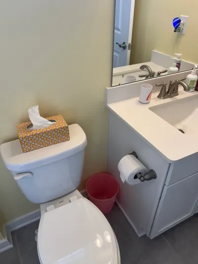 Small bathroom with white toilet, white vanity with cultured marble top, mirror, and gray tile floor.