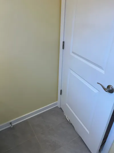 Corner of a room with sage green walls, white raised panel door, and gray large-format tile floor.