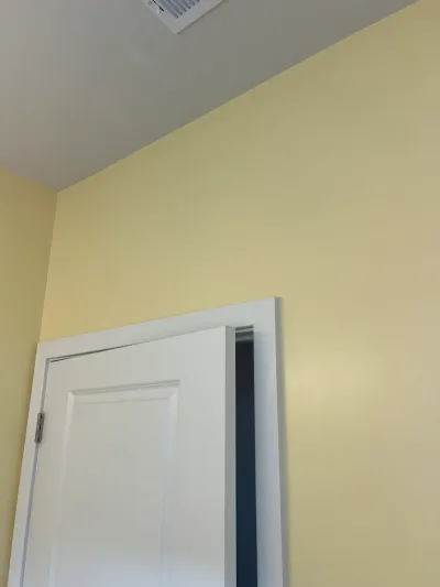 Corner of a pale yellow room with white ceiling, open white panel door, and ceiling air vent.