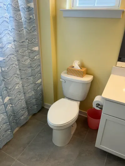 Small bathroom with white toilet, gray tile floor, yellow walls and a blue fish-print shower curtain.
