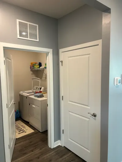 Gray hallway with white panel doors opening to a laundry room with washer, dryer and wire shelf.