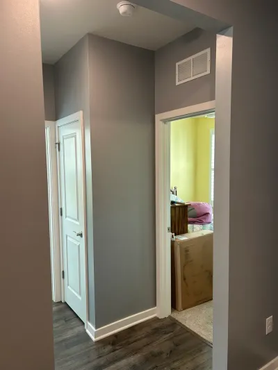 Gray painted hallway with vinyl plank flooring and white trim looking into a yellow-green bedroom.