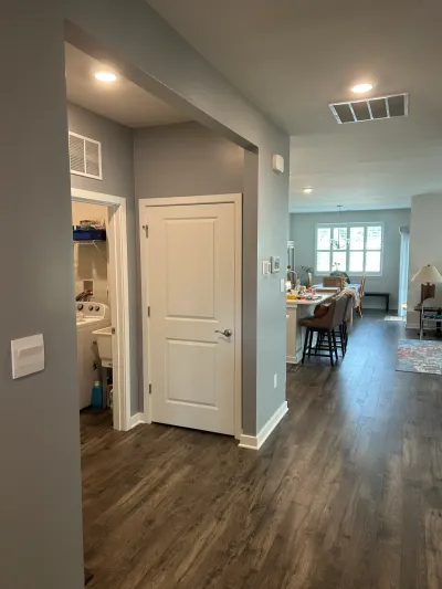 Gray hallway with dark wood-look plank flooring opening to a kitchen island, dining area and laundry room.