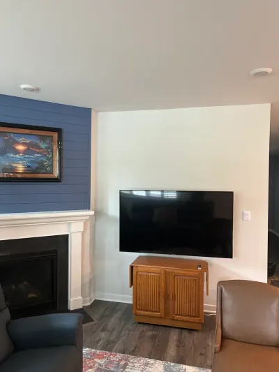 Living room corner with navy shiplap fireplace wall, white mantel, and wall-mounted TV above an oak cabinet.