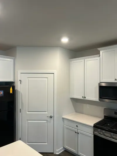 White shaker kitchen cabinets with quartz counter, stainless range and microwave beside a white panel door.