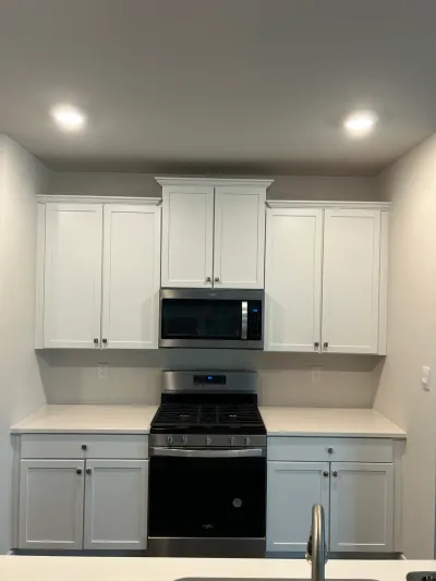 White shaker kitchen cabinets with matte black knobs around a stainless gas range and microwave.