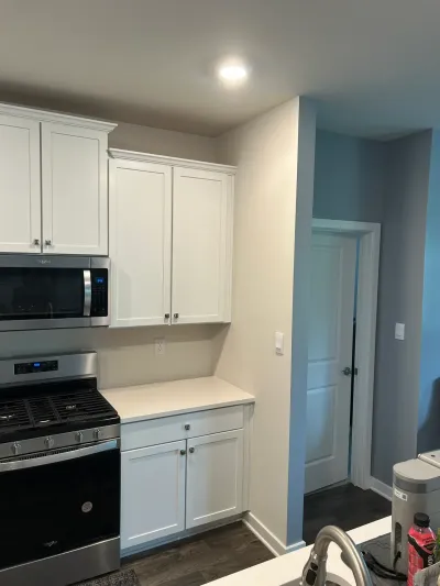 White shaker kitchen cabinets with quartz counter, stainless range and microwave, dark plank floor.