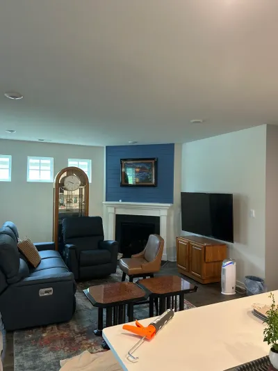 Finished basement family room with navy shiplap corner fireplace, white mantel, wall-mounted TV and leather recliners.