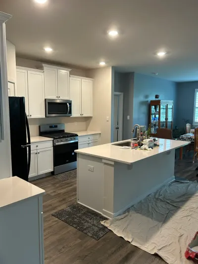 White shaker kitchen with quartz island and dark plank floors, drop cloths down during work in progress.