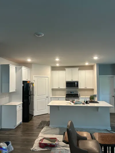 White shaker kitchen with large quartz island, stainless range and drop cloths on the floor mid-project.