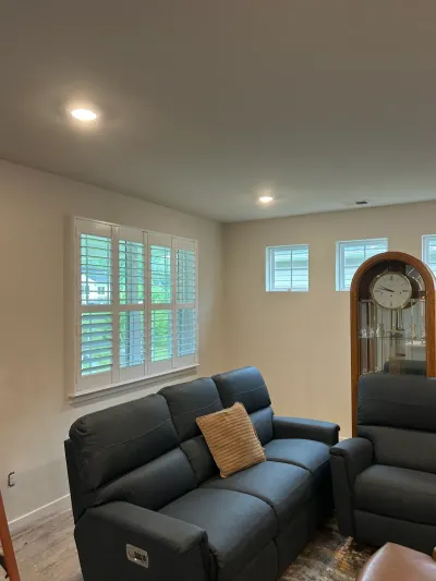 Beige living room with white plantation shutters, blue reclining sofa and tall grandfather clock.