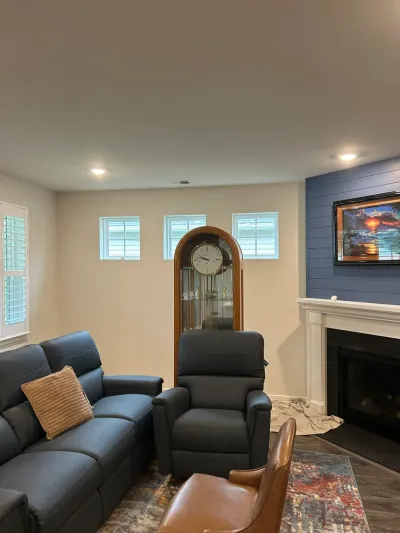 Finished basement living room with navy shiplap fireplace wall, white mantel, and gray-blue recliners.