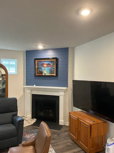 Living room with navy shiplap fireplace wall, white mantel, gas insert, and oak TV console on vinyl plank floor.