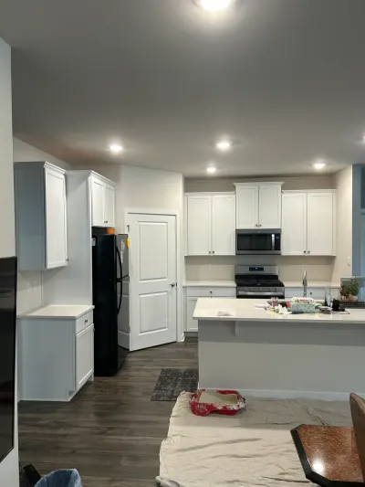 White shaker kitchen mid-painting with drop cloth, roller tray, stainless range and peninsula counter.