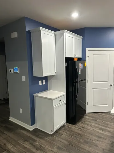 White shaker cabinets and quartz counter beside a black refrigerator against a navy accent wall.