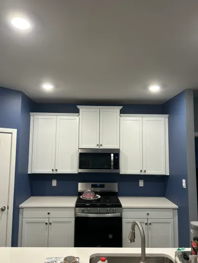 Kitchen with white shaker uppers, gray base cabinets, navy walls, stainless range and microwave.