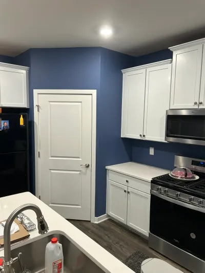 White shaker kitchen with navy walls, quartz counters, stainless gas range and dark wood-look floors.
