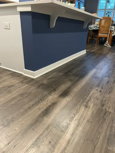 Gray wood-look vinyl plank flooring beside a navy kitchen island with white corbels and countertop overhang.