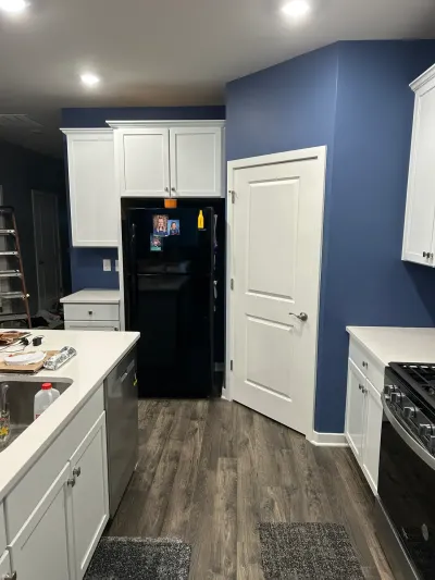 Galley kitchen with white shaker cabinets, quartz counters, navy walls and black appliances, mid-remodel.