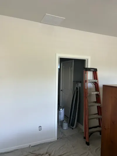 Freshly painted bedroom with drop cloth on the floor and an orange step ladder standing in the doorway.
