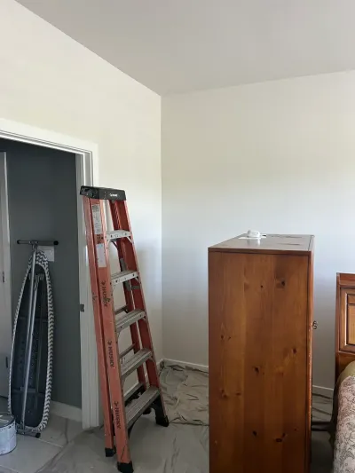 Bedroom corner mid-repaint with cream walls, gray closet interior, step ladder and drop cloths.