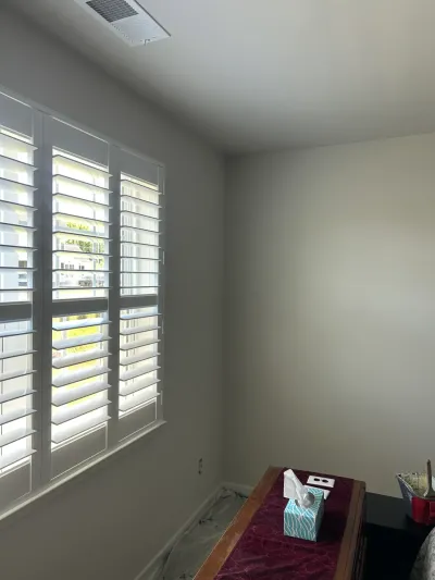 Freshly painted bedroom corner with white plantation shutters, floor protected by plastic sheeting.