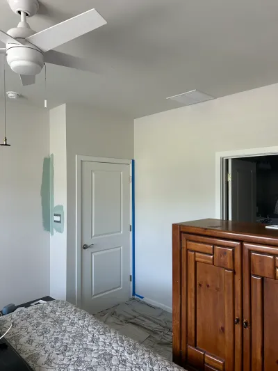 Bedroom being repainted, with taped door trim, a teal paint swatch on the wall and a drop cloth on the floor.