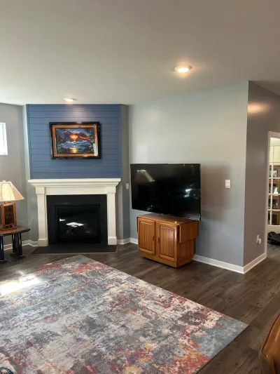 Living room with corner gas fireplace, blue shiplap chimney, white mantel, dark plank floors and mounted TV.