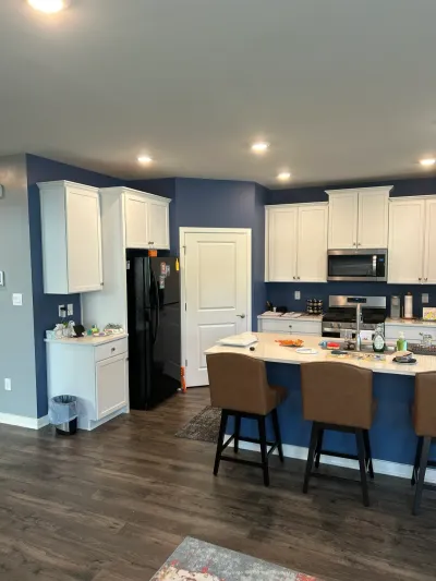 Open kitchen with white cabinets, navy walls, a seated island with leather barstools, and dark plank floors.