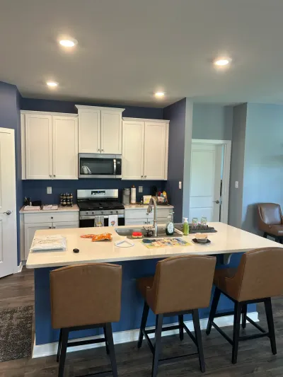 White-cabinet kitchen with navy walls, stainless range, and a white peninsula bar with three brown stools.