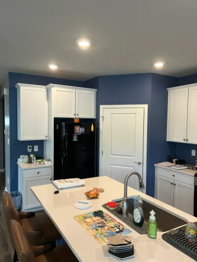 Navy blue kitchen with white shaker cabinets, quartz island with sink, and black refrigerator.