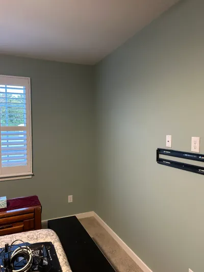 Sage green bedroom corner with a black TV wall mount installed above a low black media chest.
