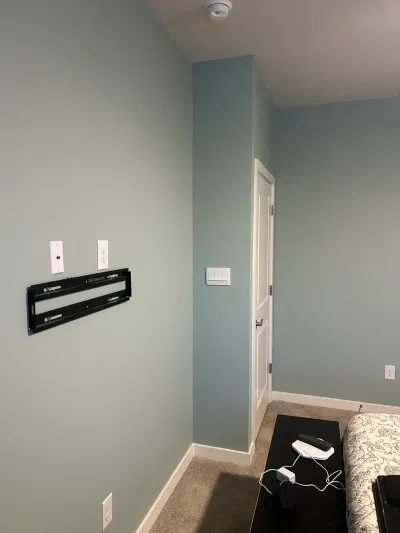 Soft blue-green bedroom corner with white trim, carpet, TV wall mount and a white door.