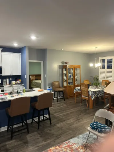 Open kitchen with white cabinets and navy peninsula flowing into a dining area with chandelier and wood floors.