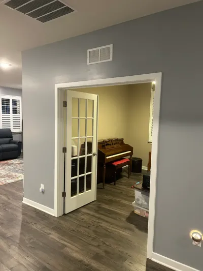 Gray hallway with white French door open to a yellow music room holding an upright piano.